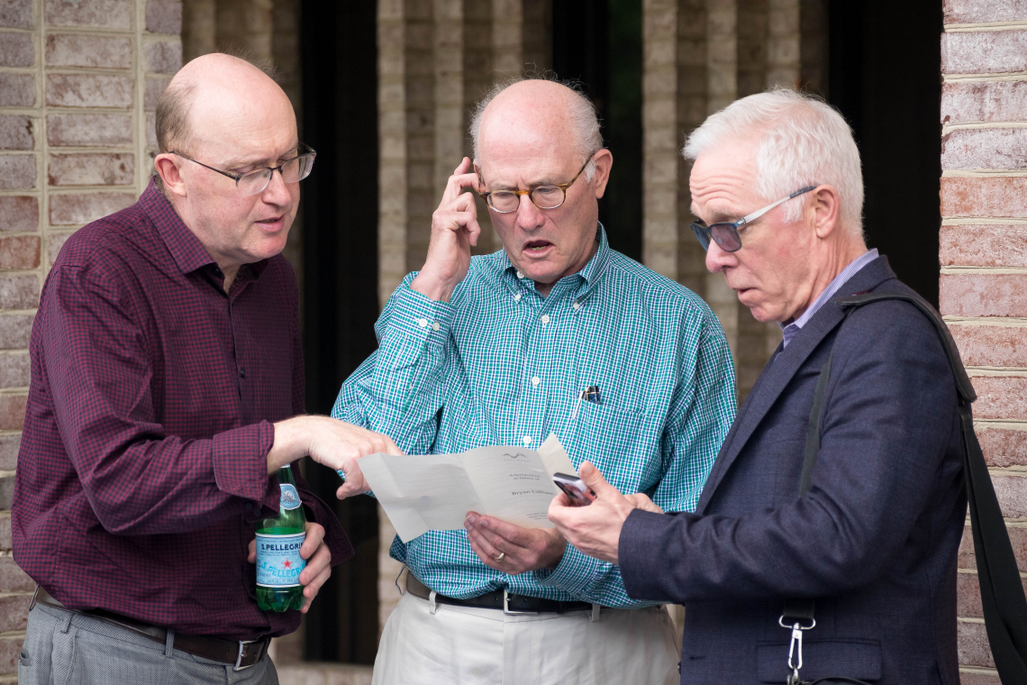 Three men looking at a program