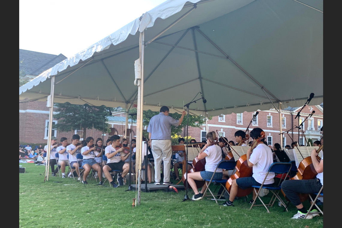 Student orchestra members playing in an outdoor tent